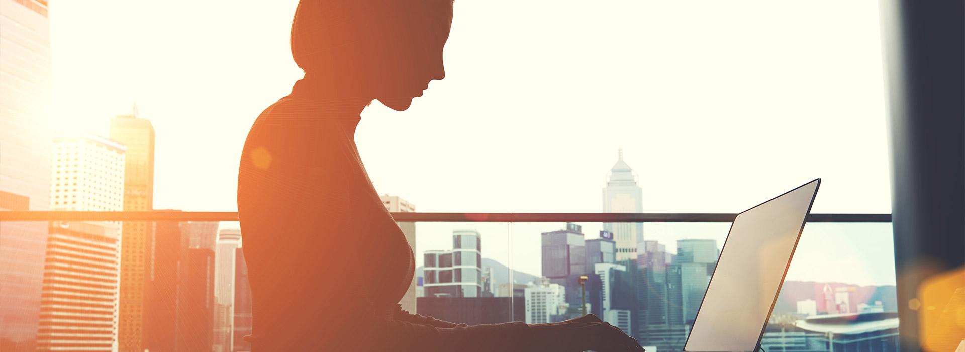 women on balcony looking at laptop with city skyline