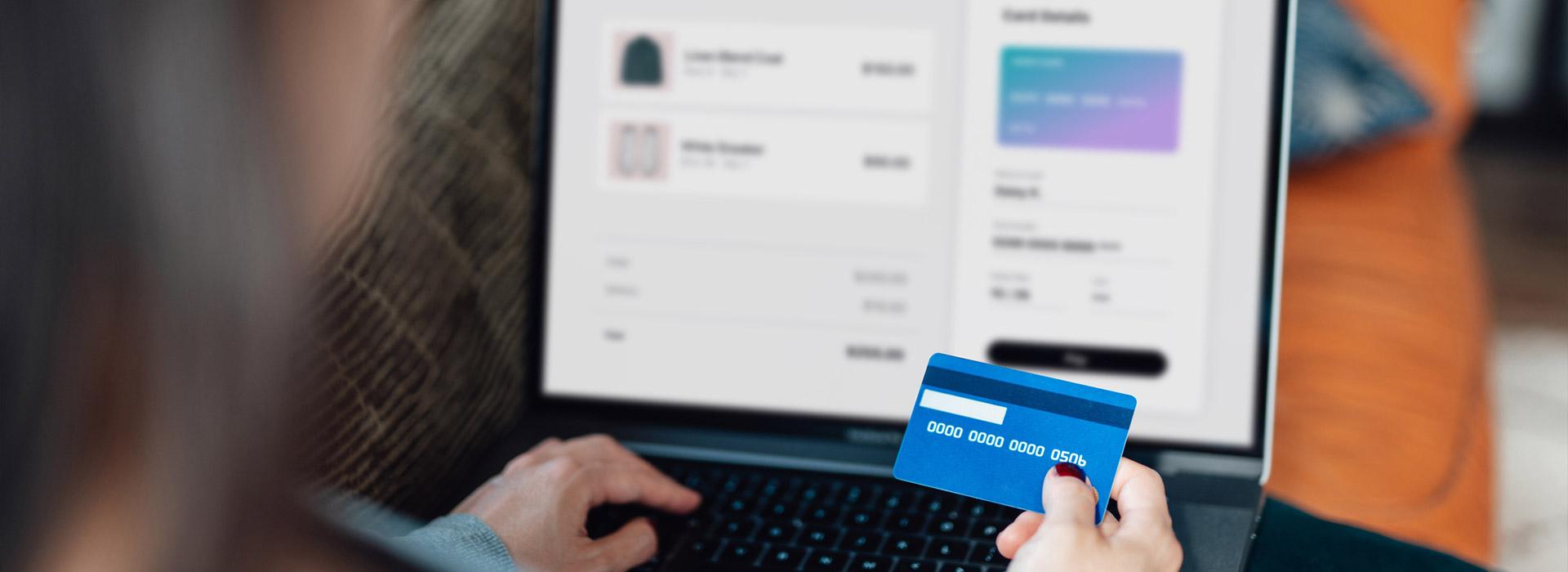 Hand holding credit card in front of computer making an electronic payment (transaction)